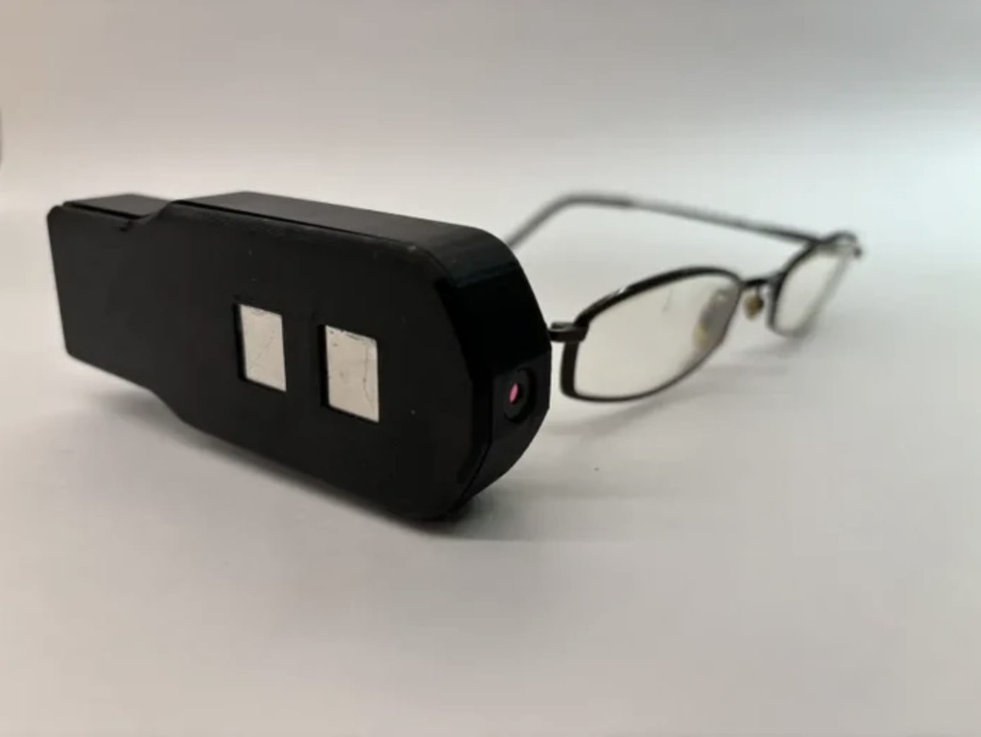 The Gen 0.2 prototype: a black case with two metal touch pads and a camera, clipped to the arm of a pair of glasses.