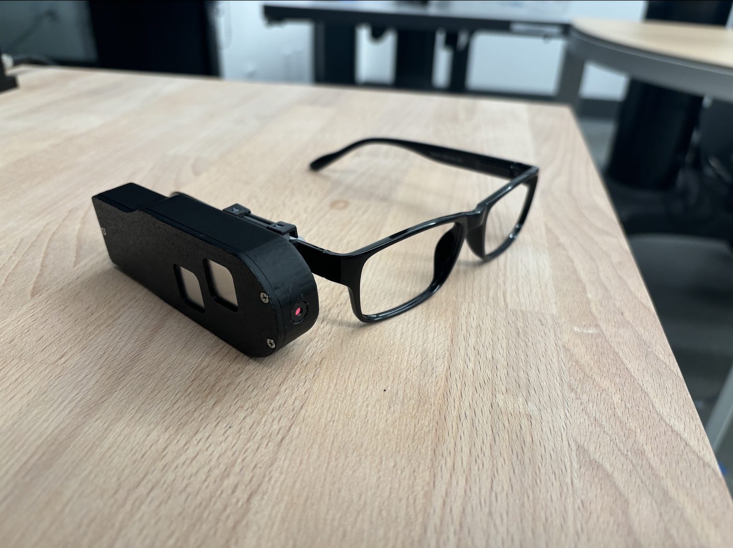 Video of the Gen 0.3 prototype working. The photo shows its black case, with two metal touch pads and a camera, clipped to a pair of glasses on a table.
